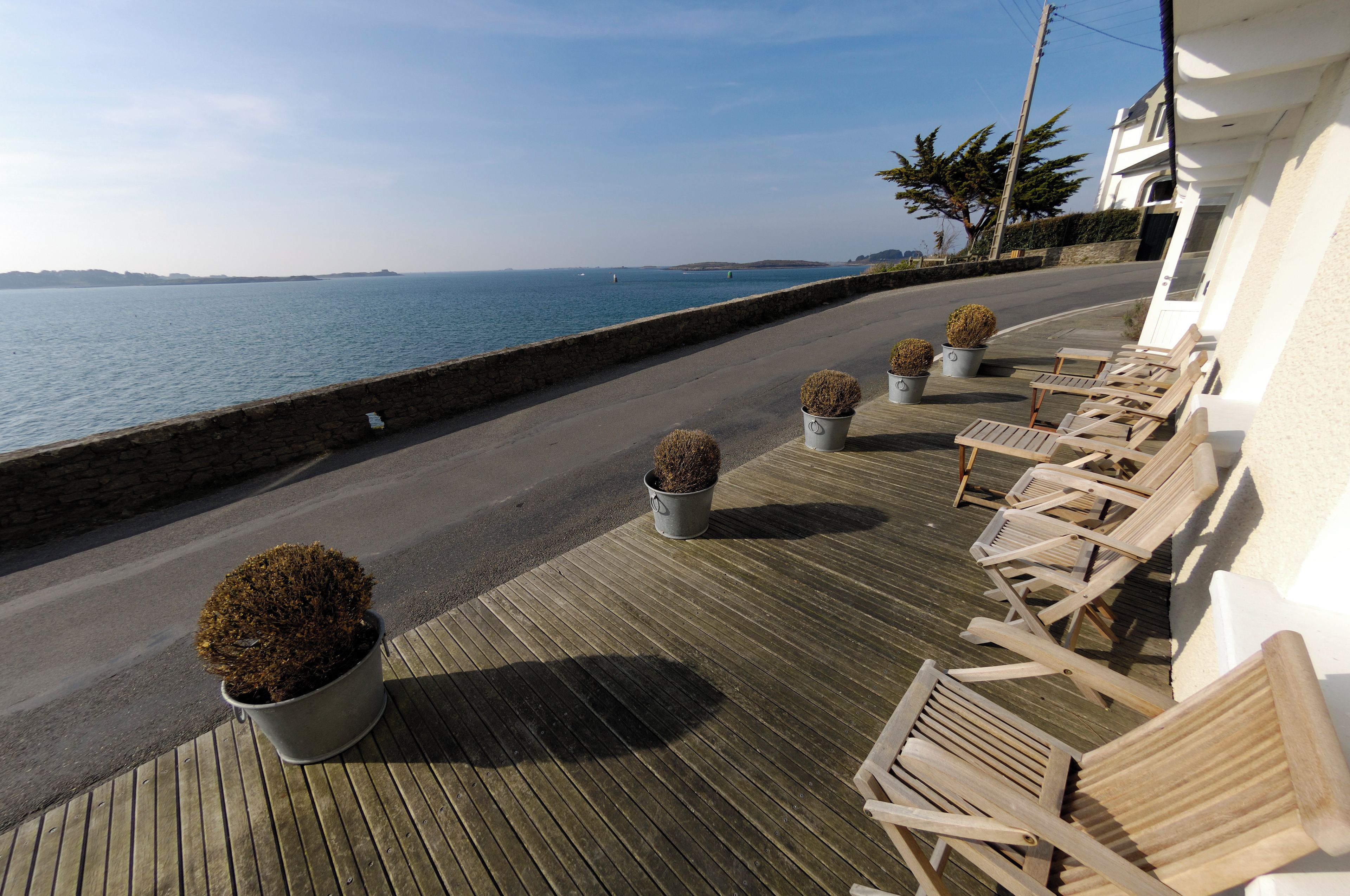 Eine Holzterrasse mit Liegestühlen und Kübelpflanzen, mit Blick auf ein Gewässer.