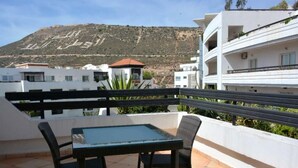 Une terrasse avec une table et des chaises, un bâtiment blanc en arrière-plan et une colline.