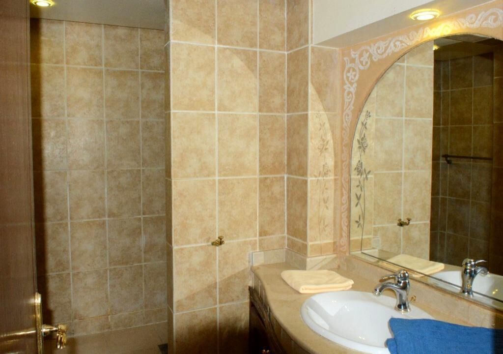 A bathroom with beige tiles, a large mirror, a white sink, and a towel on the counter.