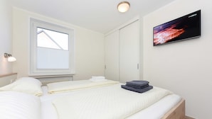 Een slaapkamer met een bed, een aan de muur bevestigde televisie, een raam en een bedlampje.