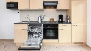 Een moderne keuken met houten kastjes, een ingebouwde magnetron, een vaatwasser, een koffiezetapparaat en een waterkoker.