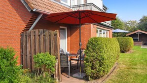 Een terras met een tafel, stoelen en een rode parasol, en een huis van baksteen.
