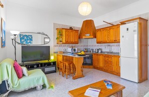 Kompakti keittiö, jossa on puiset kaapit, jääkaappi, mikroaaltouuni sekä ruokailutila, jossa on pöytä ja tuolit.