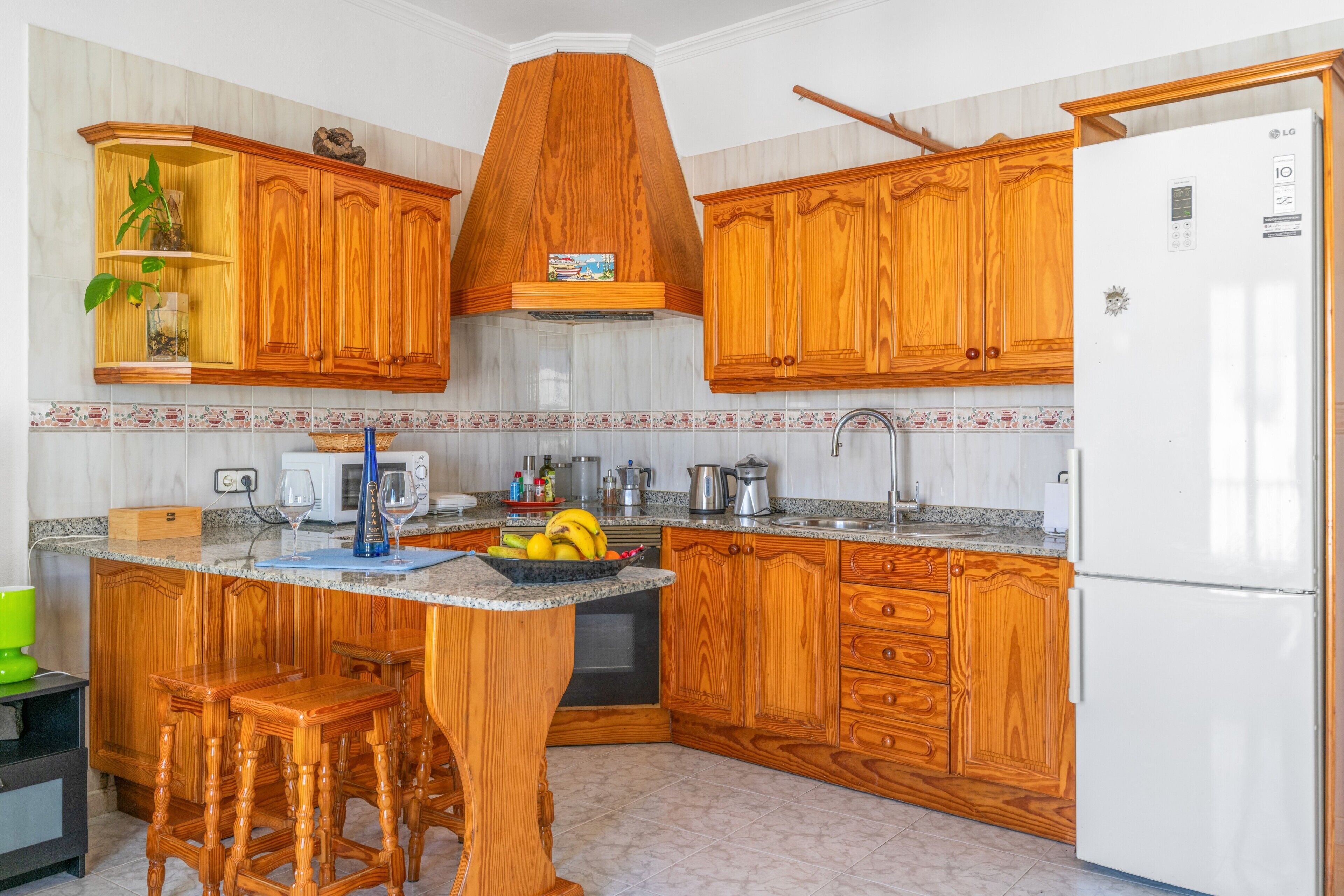Una cocina con armarios de madera, una isla central con taburetes, microondas y refrigerador.