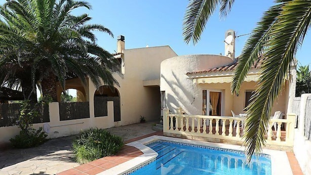 Une piscine dotée d’une terrasse carrelée, entourée d’un bâtiment blanc avec un balcon.