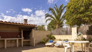 Une terrasse extérieure avec un sol en pierre, un espace barbecue et des chaises longues.