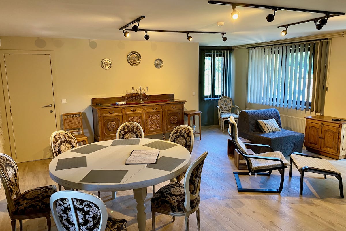 Un comedor con una mesa redonda y sillas, un aparador de madera y un sofá azul en una habitación bien iluminada con luces de techo.