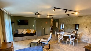 A modern living room with a sofa, dining table, chairs, and a stone wall. - Châtelet de Barbençon (Beaumont)