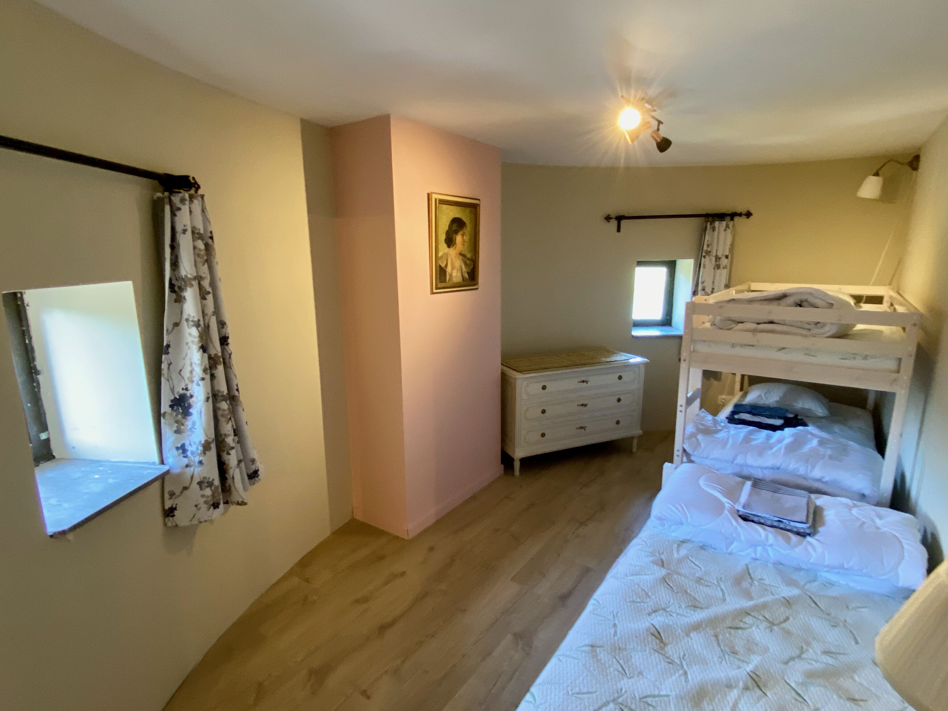 A bedroom with a bunk bed, a dresser, a window, and a painting on the wall.