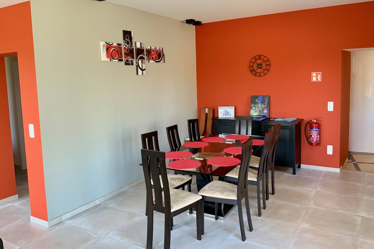 Un comedor con una mesa y sillas rojas, un reloj en la pared y un extintor.