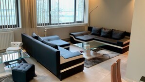 A modern living room with a sectional sofa, a glass coffee table, and a white chair. - Châtelet de Barbençon (Beaumont)