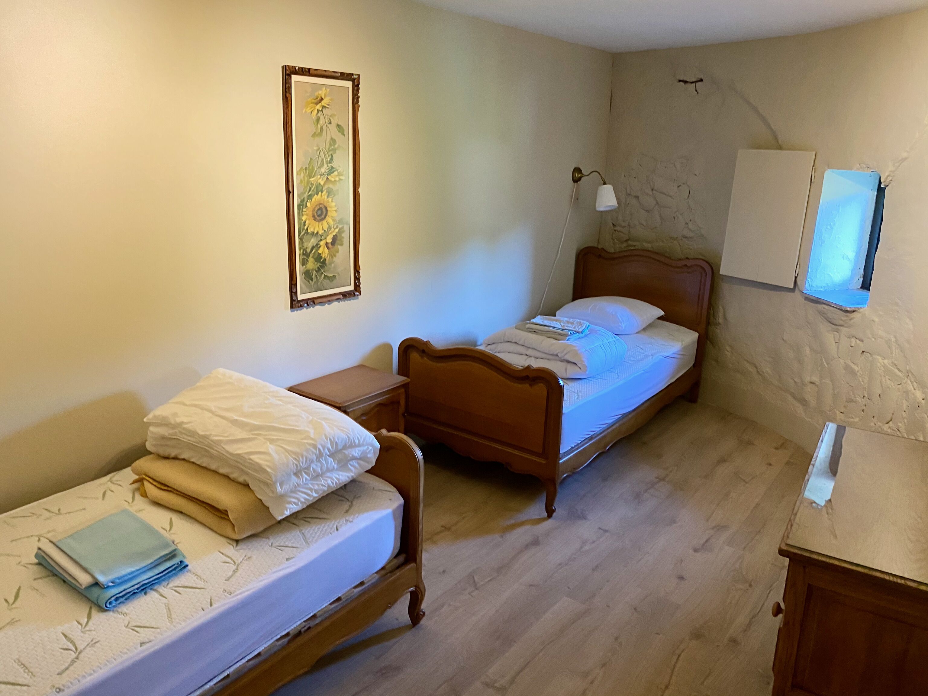 A bedroom with two wooden beds, a nightstand, a bedside lamp, a wall-mounted TV, and a framed floral painting.