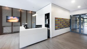 Ein moderner Empfangsbereich mit einem weißen Empfangstresen, einem Wandfernseher und einer farbenfrohen Wanddekoration.