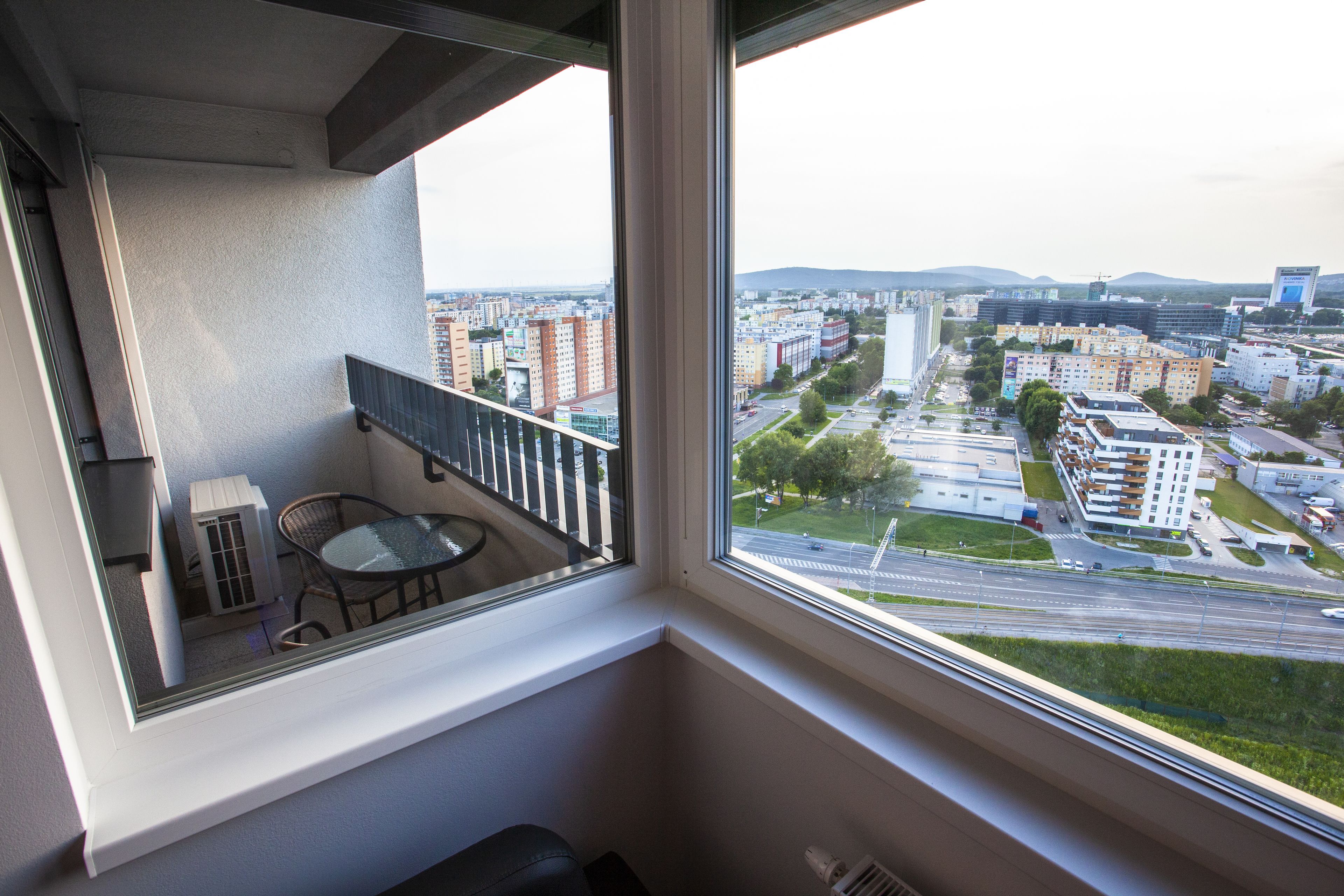 Uma varanda com mesa e cadeiras, com vista para um horizonte urbano com edifícios e uma estrada.