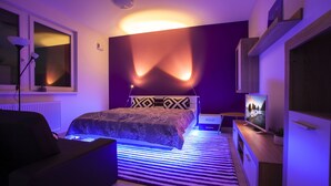 Ein modernes Schlafzimmer mit Bett, Fernseher, Schreibtisch und Fenster.