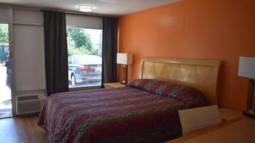 A hotel room with a bed, a bedside table, a lamp, and a view of the street through the window.