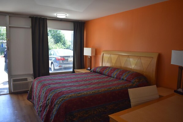 A hotel room with a bed, a bedside table, a lamp, and a view of the street through the window.