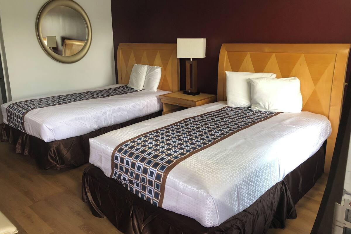 Two single beds with patterned bedspreads, a bedside table with a lamp, and a round mirror on the wall.