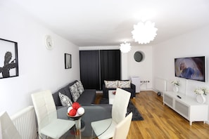 A modern living room with a sofa, chairs, a glass coffee table, a TV, and a fireplace.