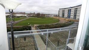 A balcony with a view of a grassy area, a river, and a multi-story building. - 2 Beds Riverview Tideslea Apartment (London)