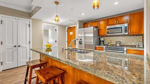 A kitchen with granite countertops, stainless steel appliances, wooden cabinets, and two bar stools.