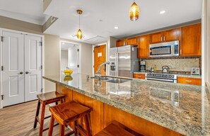 A kitchen with granite countertops, stainless steel appliances, wooden cabinets, and two bar stools.