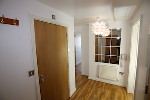 A hallway with wooden flooring, a wooden door, a white radiator, and a wall-mounted light fixture.