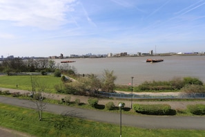 A riverside view with a pedestrian path, a bridge, and a distant city skyline.
