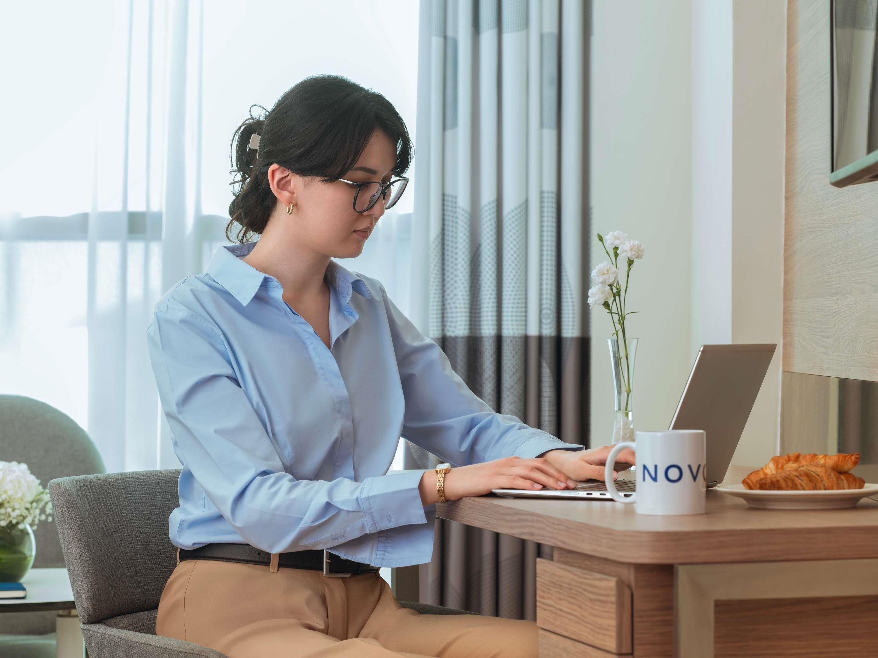 Une personne est assise à un bureau, devant un ordinateur portable, avec une tasse et une assiette remplie de viennoiseries.