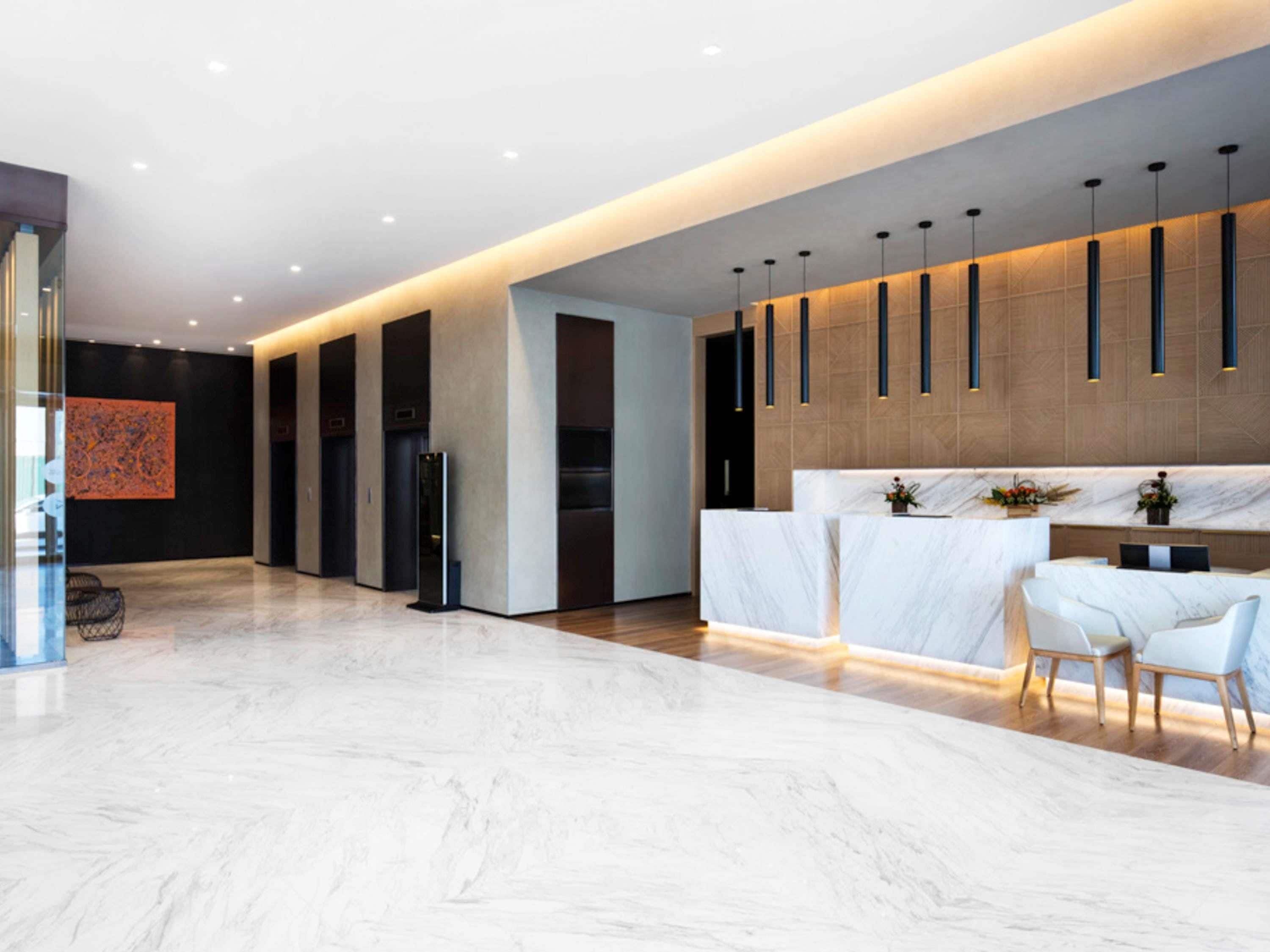 A modern hotel lobby with a marble floor, a reception desk, and a seating area.