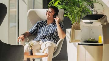 A person sitting in a modern chair with a plant and a small table with a drink and a plate of food.