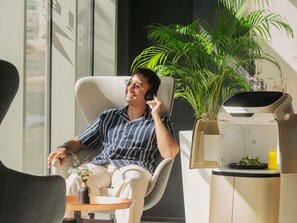 A person sitting in a modern chair with a plant and a small table with a drink and a plate of food. - Novotel Bur Dubai (Dubai)