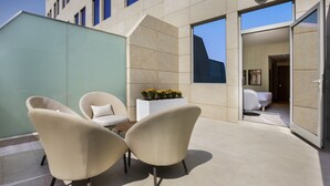 A modern outdoor seating area with two chairs and a table, a planter with flowers, and a view into the building. - Novotel Bur Dubai (Dubai)