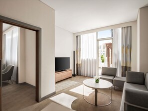 A modern hotel room with a flat-screen TV, a round coffee table, a sofa, and a chair. - Novotel Bur Dubai (Dubai)
