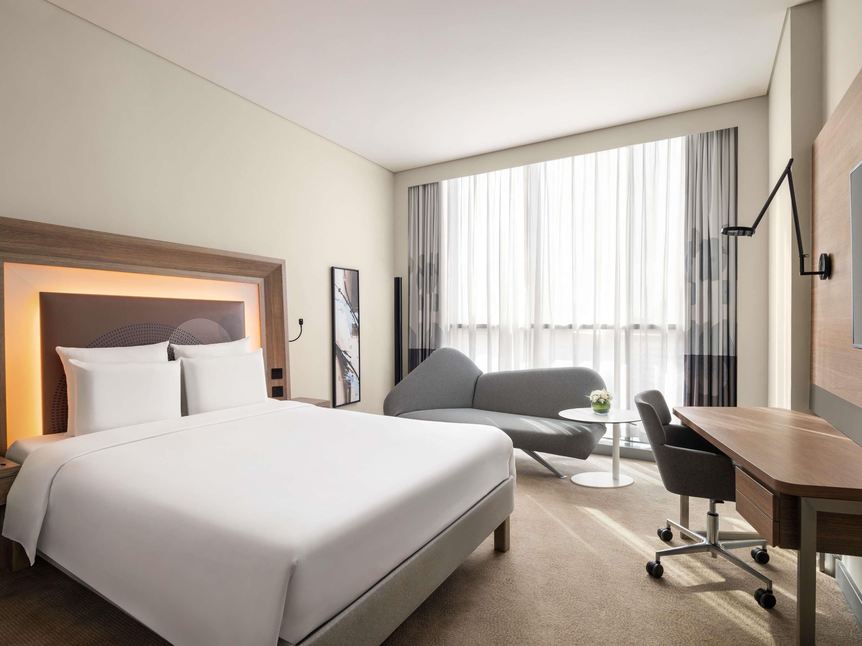 A hotel room with a large bed, a desk, a chair, and a sofa.