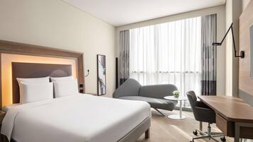 A hotel room with a large bed, a desk, a chair, and a sofa.