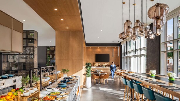 A modern kitchen with a long counter, bar seating, and a large TV screen. - Novotel Bur Dubai (Dubai)
