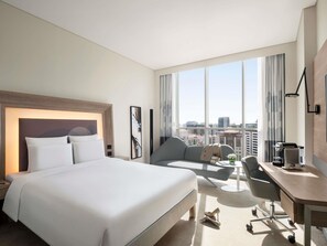 A hotel room with a large bed, a desk, a chair, and a view of the city. - Novotel Bur Dubai (Dubai)