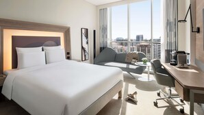 A hotel room with a large bed, a desk, a chair, and a view of the city. - Novotel Bur Dubai (Dubai)