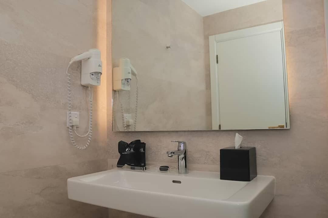 Een badkamer met een witte wastafel, een haardroger, een spiegel en een deur.