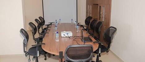 A conference room with a long table, black office chairs, water bottles, and a projector screen.