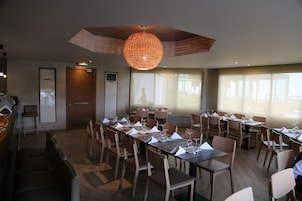 Un comedor con mesas largas dispuestas para una comida, sillas de madera y una lámpara colgante grande.