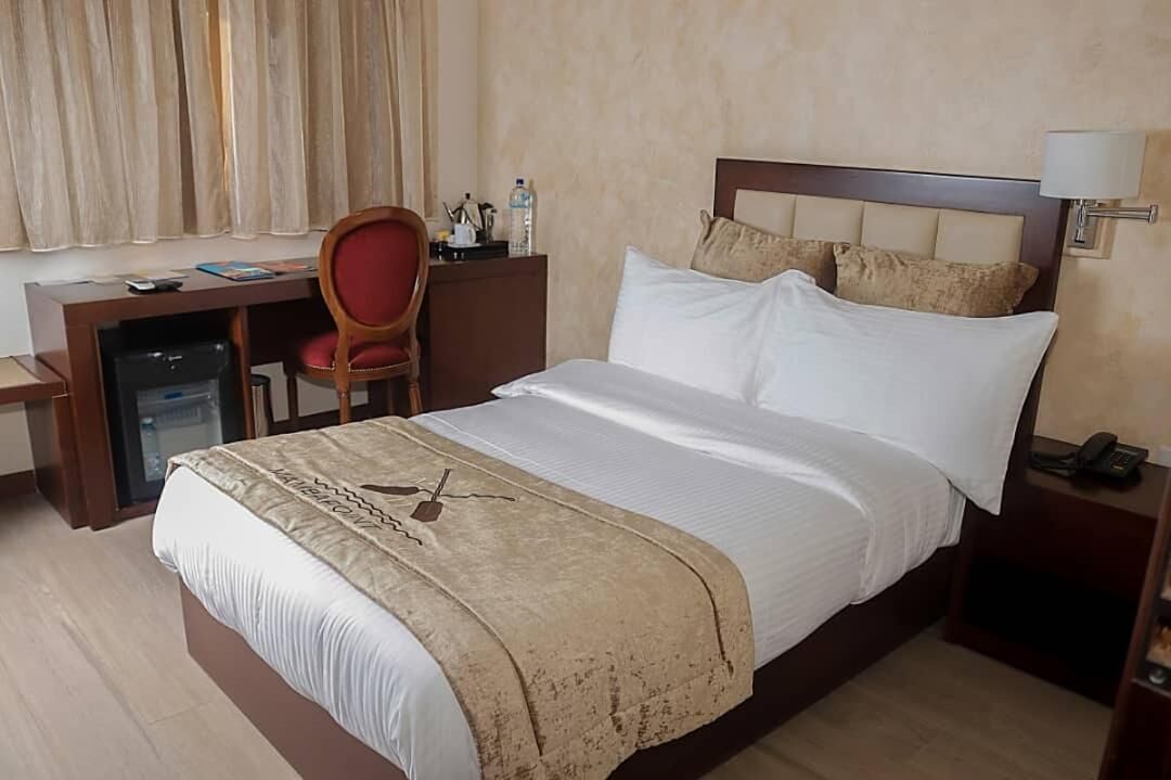 A hotel room with a bed, a desk, a chair, a lamp, and a telephone.