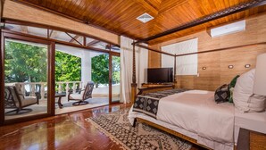 A spacious bedroom with a large bed, a television, and a view of the outdoors through sliding glass doors. - Blue Jewel Oceanfront Private Villa (Tamarindo)