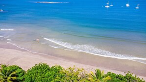 A beach with clear blue water, a sandy shore, and some greenery in the foreground. - Blue Jewel Oceanfront Private Villa (Tamarindo)