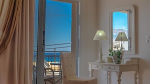 Una habitación con balcón, un tocador blanco con espejo, dos lámparas y un jarrón con flores.