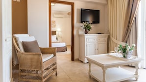 Una habitación de hotel con una silla de mimbre, una mesa blanca, un televisor, un armario y una cama.