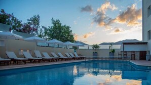 Una piscina con sillas de descanso y sombrillas, rodeada por un edificio con vistas a la montaña.