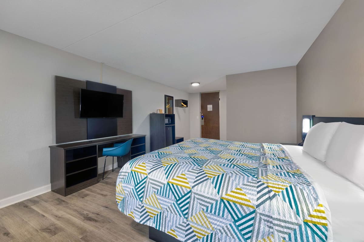 Habitació d'hotel amb un llit gran, una taula de treball amb una cadira, una televisió pantalla plana penjada a la paret i un armari.