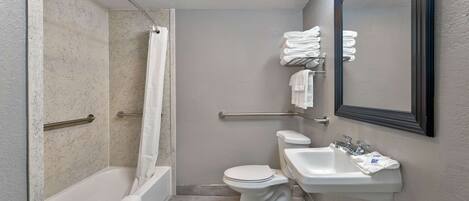 A compact bathroom with a bathtub, toilet, and sink, equipped with a handrail and a mirror.